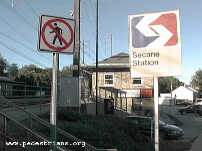 Photo - A No Pedestrian Crossing sign by a train station.